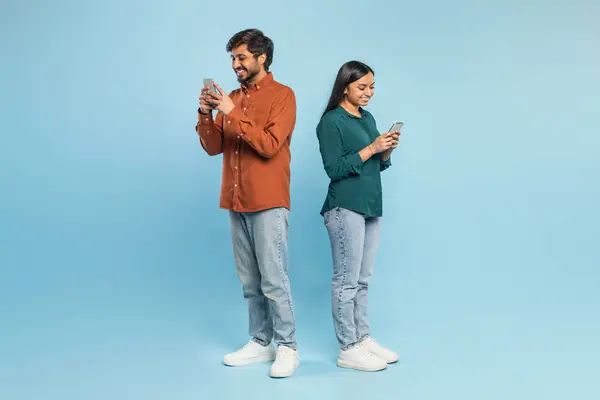 迷人的印度夫妇背靠背地站着 用他们的智能手机 象征着现代通信 — 图库照片