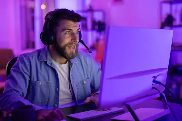 Człowiek Słuchawkami Intensywnie Skupiony Ekranie Komputera Otoczony Nastrojowym Niebieskim Oświetleniem — Zdjęcie stockowe