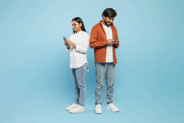 インド人男性と女性は 青い背景に対して互いを無視して 携帯電話に囲まれた側に立っています — ストック写真