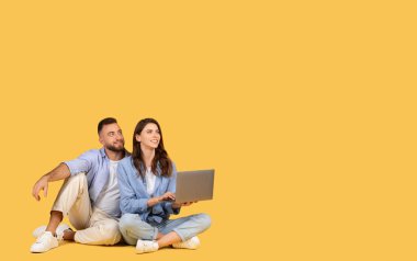 Rahatlamış bir adam ve kadın yan yana oturuyor, dizüstü bilgisayar kullanıyor ve dikkatlice başka yere bakıyor.