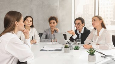 Beş profesyonel kadından oluşan bir grup, iyi aydınlatılmış bir ofiste konferans masasında bir tartışmaya giriştiler.