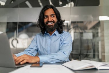 Kendine güveni tam bir erkek, iş yerinde dizüstü bilgisayarla oturuyor, karizma yayıyor ve yakınlık gösteriyor.