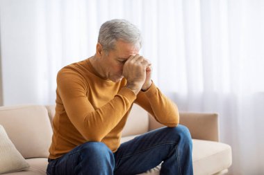 Düşünceli bir son sınıf öğrencisi hardal süveter giyer ve kafasında derin bir düşünce ya da endişeye işaret eder.