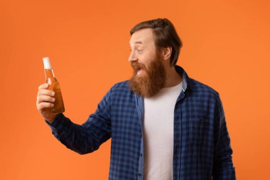 Kızıl saçlı neşeli sakallı adam elinde bir şişe bira tutarken neşeli bir şekilde bağırıyor. Haftasonu partisinin sevincini ve neşesini yayıyor. Portakal rengi stüdyo arka planında bir portre.