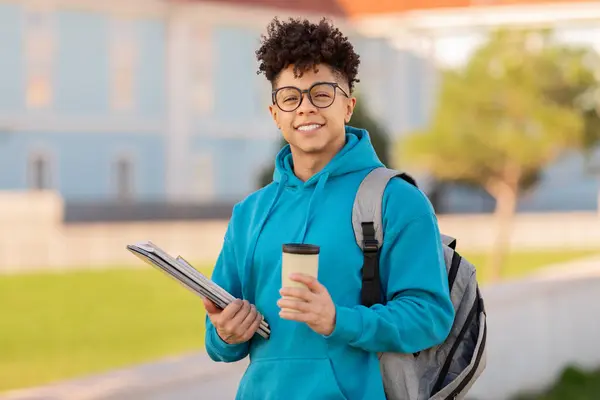 一个心满意足的巴西学生站在室外 手里拿着课本和咖啡杯 背着背包 站在一所大学前面 — 图库照片