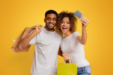Afrikalı-Amerikalı alışveriş alışveriş torbaları ve kredi kartı, turuncu arka plan ile mutlu neşeli