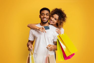 Banka kredi kartı ve turuncu zemin üzerine alışveriş torbaları da kucaklayan, Afrikalı-Amerikalı çift shopaholics, memnun