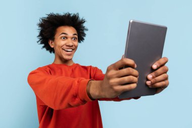 Afro-Amerikalı mutlu bir adam dijital tabletle selfie çekiyor ve şaşkınlığını dile getiriyor.