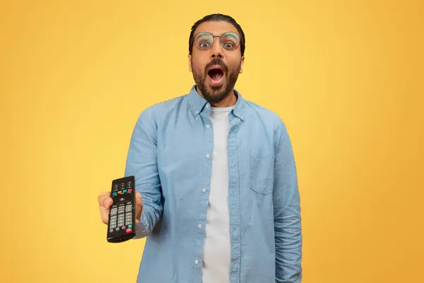 Surprised Indian Man Holding Remote Control Expressing Shock Yellow Background — Stock Photo, Image