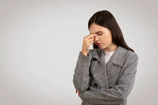 頭痛でストレスの兆候を示すチェッカーブレーザーの女性 彼女の鼻の橋をピンチ ミニマリストグレーの背景に対して フリースペース — ストック写真