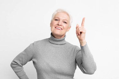 A cheerful senior, elderly European woman with one finger raised, suggests having an idea or point to make, reflecting s3niorlife wisdom clipart