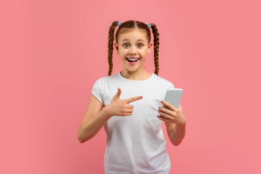 Young girl with braided hair excitedly points to her smartphone on a pink background, expressing surprise and delight clipart