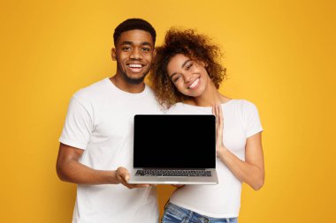 Dizüstü bilgisayar boş ekran, turuncu studio arka plan ile tutarak aşık genç Afro-Amerikan çift