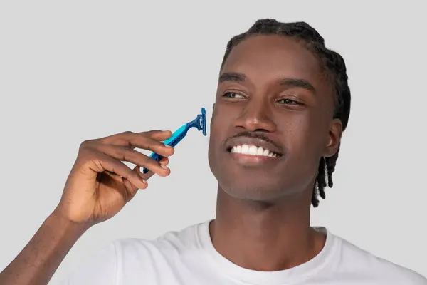 一个快乐的非裔美国男人用蓝色剃须刀刮脸的特写镜头 描绘了一个正在打扮的男人 — 图库照片