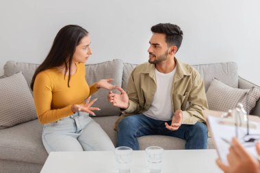 Nişanlı bir çift, danışmanlık ofisinde anlamlı el hareketleriyle ciddi bir tartışmada resmedilir.