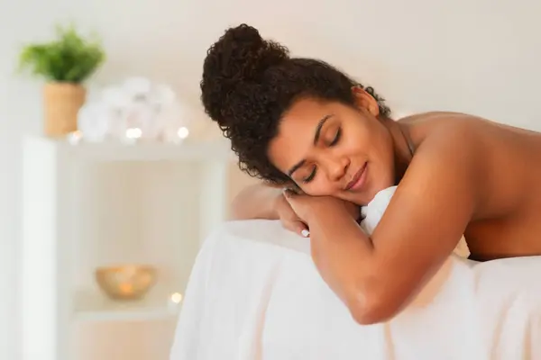 African American woman with closed eyes embraces a pillow, appearing serene and relaxed on a spas massage table