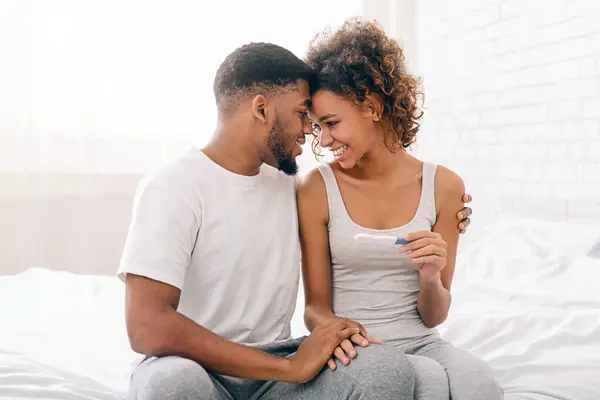 Happy couple holding positive pregnancy test, enjoying future parenthood in bed