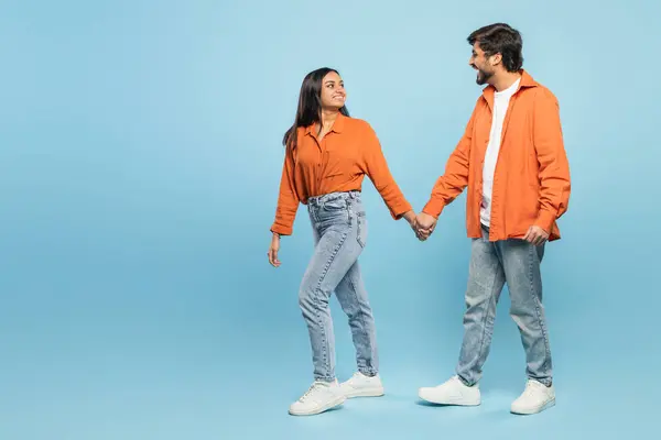 Indian man and woman in casual wear holding hands and exchanging a tender look full of connection on blue