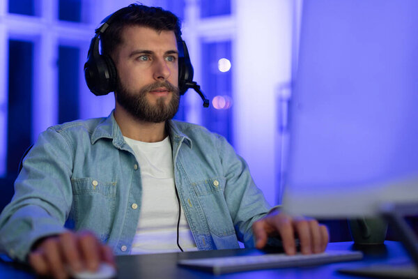 Человек сосредоточился на экране во время игр в ночное время дома, с синим светом и носить гарнитуру