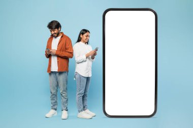 Hintli erkek ve kadın, büyük bir akıllı telefon modelinin yanında, mavi üzerinde kopya alanı için boş bir ekran sergiliyorlar.