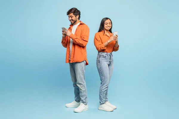 インド人男性と女性が背中に立ち 彼らのスマートフォンに深く従事し カジュアルなオレンジ色のシャツを着ています — ストック写真