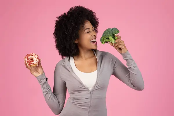 Smiling African American Woman Torn Choice Healthy Broccoli Tempting Doughnut — Stock Photo, Image
