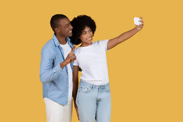 スタイリッシュな衣装を持つアフリカ系アメリカ人の若いカップルは 一緒に楽しい瞬間をキャプチャし セルフィーのためにポーズしています — ストック写真