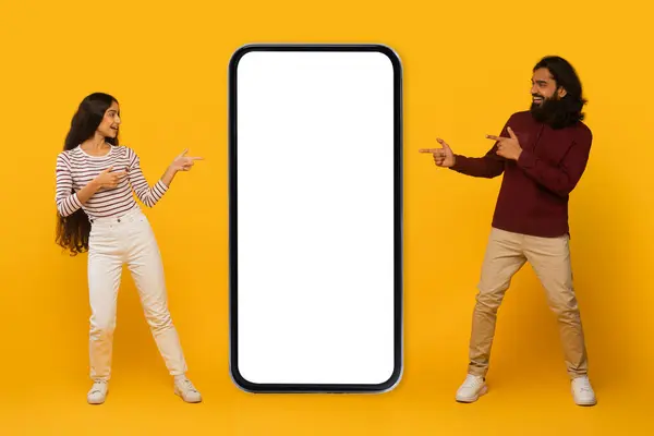 笑顔の男性と女性が交流し 黄色い背景に空白のスマートフォン画面を指差します — ストック写真