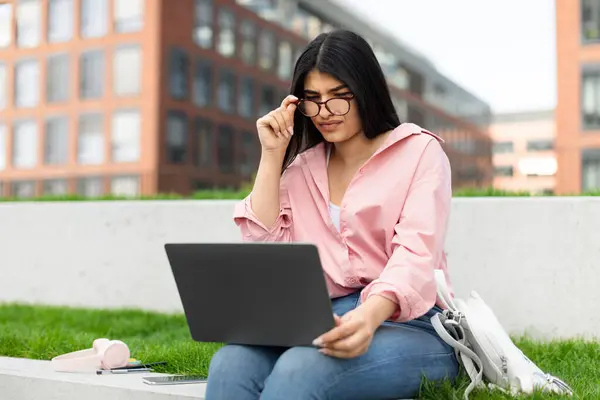 Młoda Dziewczyna Okularach Koncentruje Się Ekranie Laptopa Siedząc Zewnątrz Trawiastym — Zdjęcie stockowe