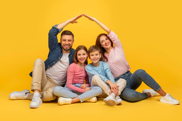Family sitting on the floor, kids between parents, making a house roof shape with their hands together on a bright yellow background