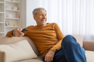 Günlük kıyafetli yaşlı bir adam elinde uzaktan kumandayla rahat bir şekilde kanepede uzanıyor. Bu da boş zamanı ya da emeklilik aktivitelerini gösteriyor.