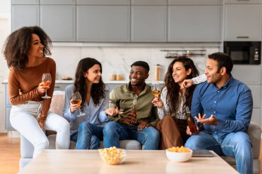 Bir grup farklı arkadaş, evde şık bir mutfak ortamında içki içerken sohbet etmekten zevk alıyor.