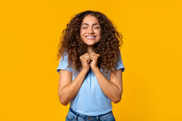 Excited Young Curly Woman Clasped Hands Expressing Joy Anticipation Yellow — Stock Photo, Image