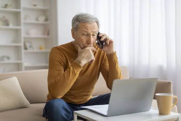 Starszy Pan Koncentrujący Się Rozmowie Telefonicznej Laptopem Otwartym Przed Nim — Zdjęcie stockowe