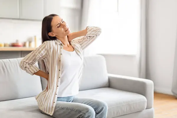 Brunette Lady Sitting Couch Home Rubbing Her Neck Lower Back — Stock Photo, Image