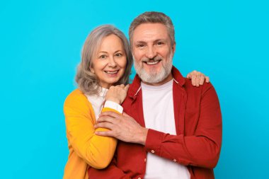 Evlilik, mutlu ortaklar. Olgun bir erkek ve kadının portresi duygusal bir anı paylaşıyor, mavi stüdyo arka planında mutluluğu kucaklıyor ve yayıyor. Sevgili son sınıf çifti.