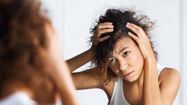 Afro-Amerikan kız çatık ve ayna yüzüne dikkatle bakıp. Saç ve sculp sorunları kavramı