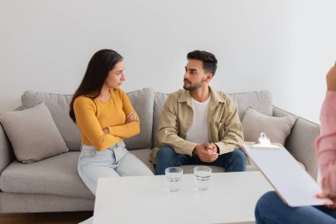 Genç bir çift kanepede gergin bir şekilde otururken, pano gözlemleyen bir terapist aile seansları sırasında terapi ve destek sağlıyordu.