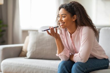 Afro-Amerikalı bir bayan akıllı telefonuyla hoparlör kipini kullanarak konuşuyor, evde ellerini kullanmadan sohbet ediyor.