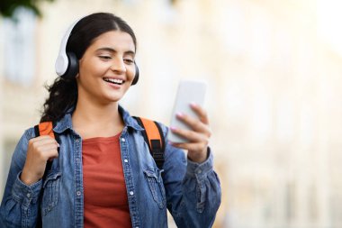 Doğulu genç bir kız öğrenci gülümseyip telefonuna bakıyor. Geleneksel eğitimle modernliği birleştiriyor. Zoomers kampüsündeki yaşam tarzını gösteriyor.