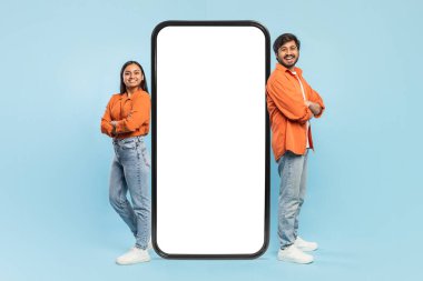 Sırtları kameraya dönük Hintli bir adam ve kadın, dev bir akıllı telefonun yanında, teknoloji temalarını resmediyorlar.