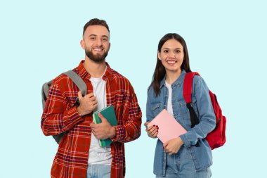Genç bir adam ve bir kadın mavi bir arka plana karşı duruyorlar, sırt çantaları ve ders kitaplarını tutuyorlar, kolej arkadaşlığı ve hazırlık hissi veriyorlar.