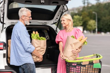 Elderly couple engaged in loading grocery bags into their car, depicting independence and active lifestyle for seniors clipart