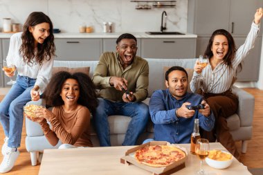 Çok ırklı genç arkadaşlar canlı bir ev ortamında heyecan ve atıştırmalıklarla video oyunları oynuyorlar.