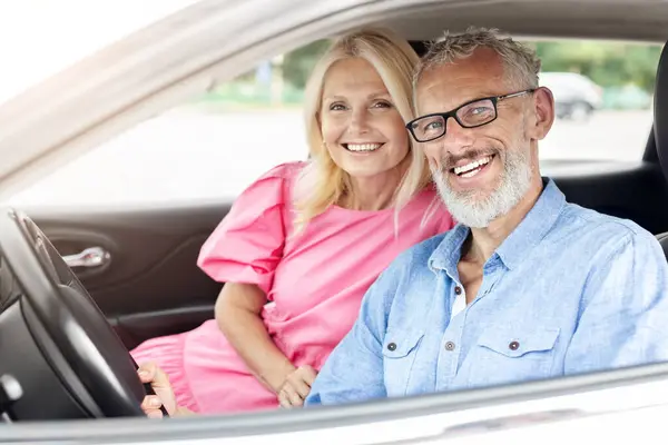 An affectionate retired married couple shares a happy moment together in their car with the senior man driving and the woman smiling warmly