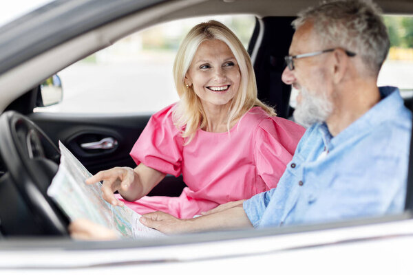 Пожилая пара на пенсии планирует свой маршрут с картой в машине, изображая чувство приключений и общения