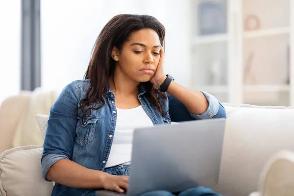 一位非洲裔美国女士在家里使用笔记本电脑时显得神魂颠倒 暗示出她需要专心致志或忧虑 — 图库照片
