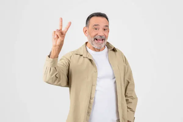 stock image Smiling elderly man making a peace sign with his hand, isolated on a white background, conveys a laid-back and happy demeanor