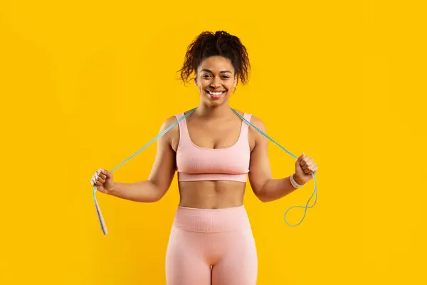 快乐的非洲裔美国女士展示了一种带跳绳的健身套路 强调力量 与黄色背景隔离 — 图库照片