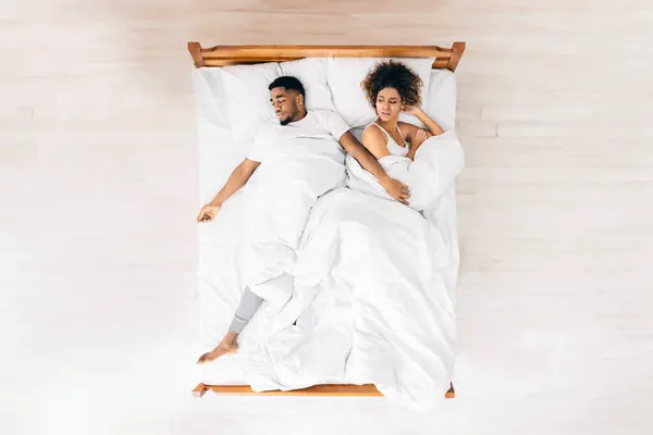 Uncomfortable dream. Upset black woman suffering from her sprawled man in bed, top view with empty space